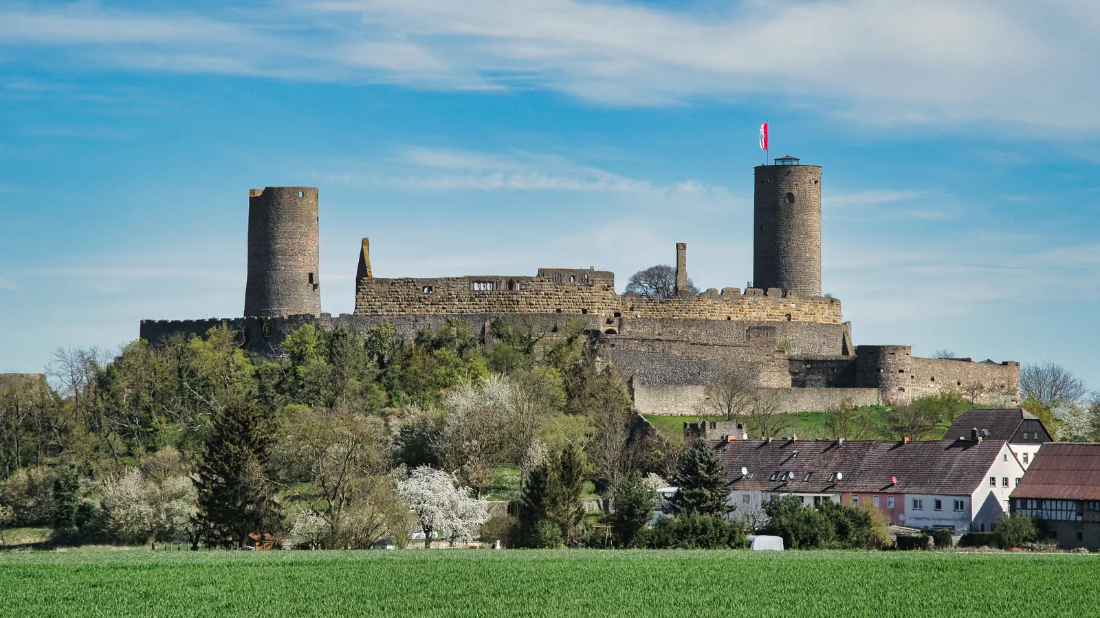 Die Burgruine Münzenberg mit ihren zwei Bergfrieden über Bäumen, Dächern und einem Feld in der Wetterau